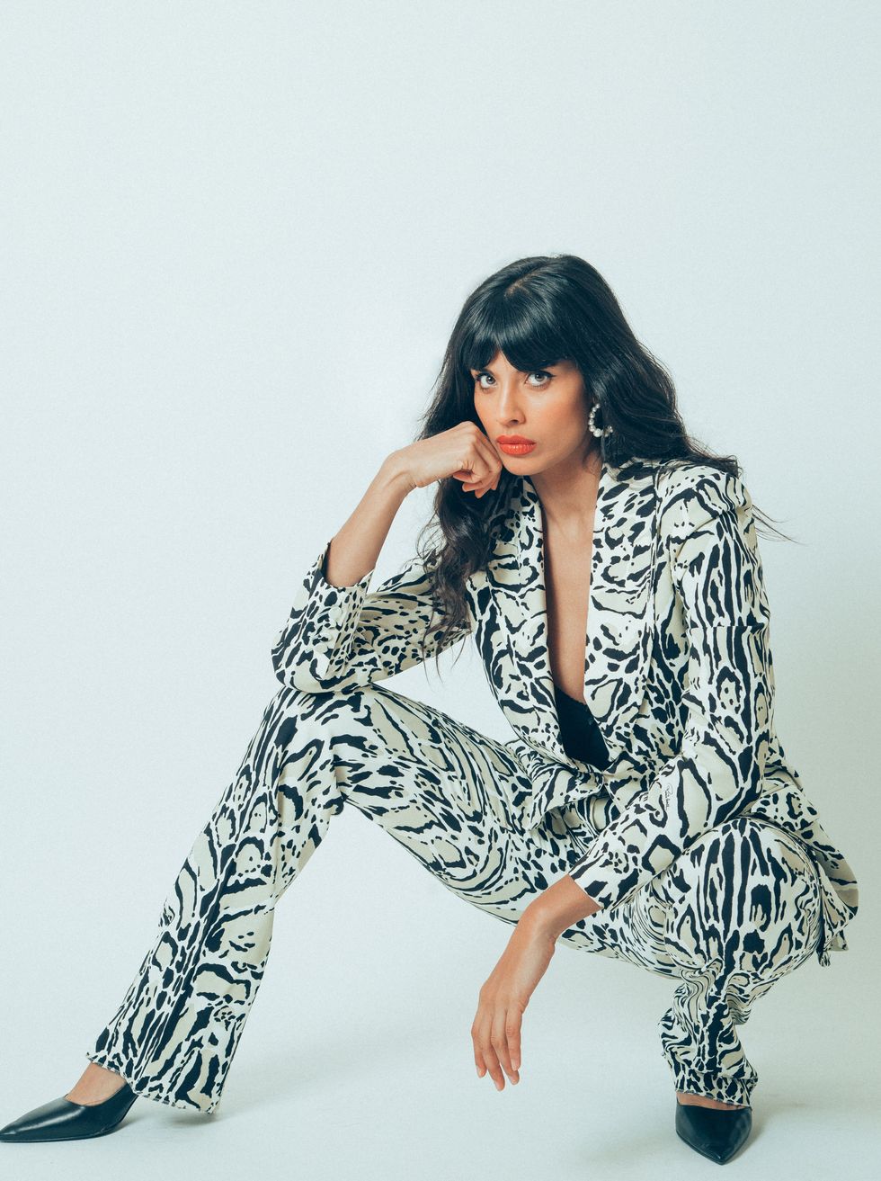 A woman with long dark hair wears a black and white animal print suit, and stares at the camera.