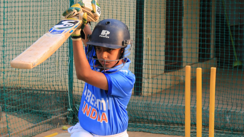 A young boy plays cricket in the nets, wearing a cricket helmet