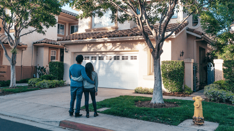 A young couple standing outside the garage of a home