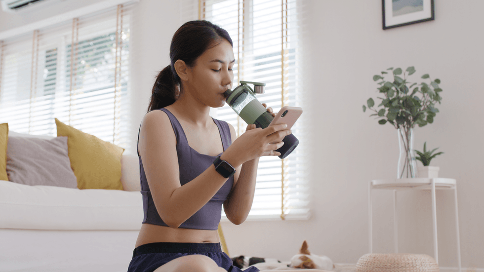A young girl looking at her phone and sipping from a water bottle