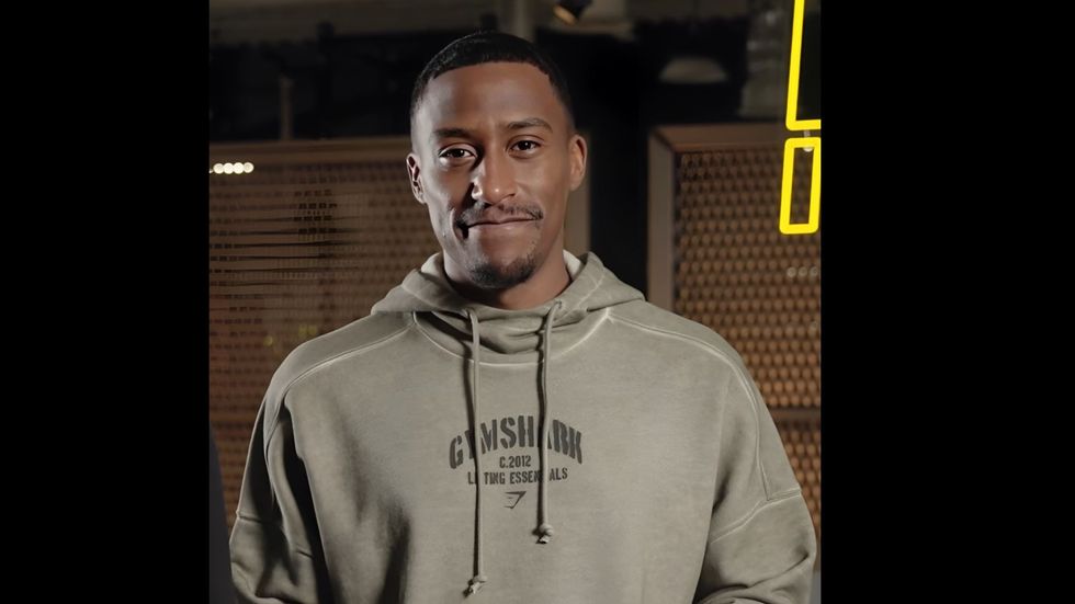 A young man in a grey hoodie smiles at the camera