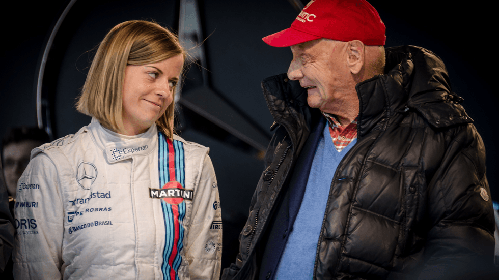 A young woman in a racing jumpsuit with an older man wearing a red cap