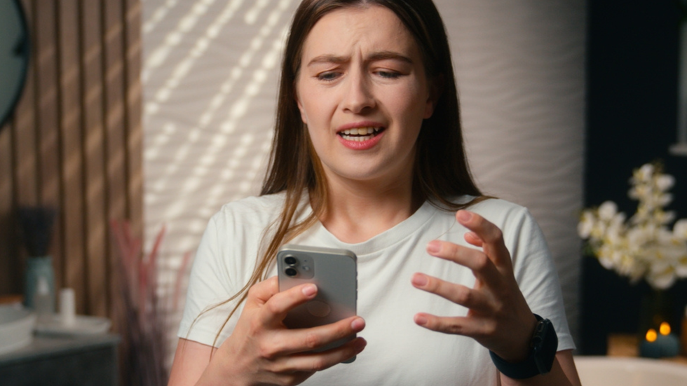 A young woman looks at her phone and grimaces