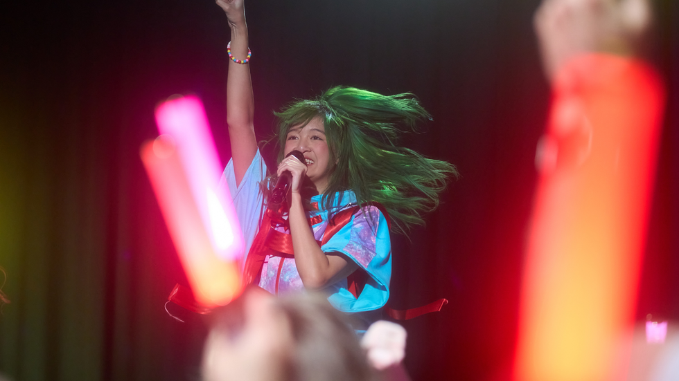 A young woman with green hair sings into a microphone