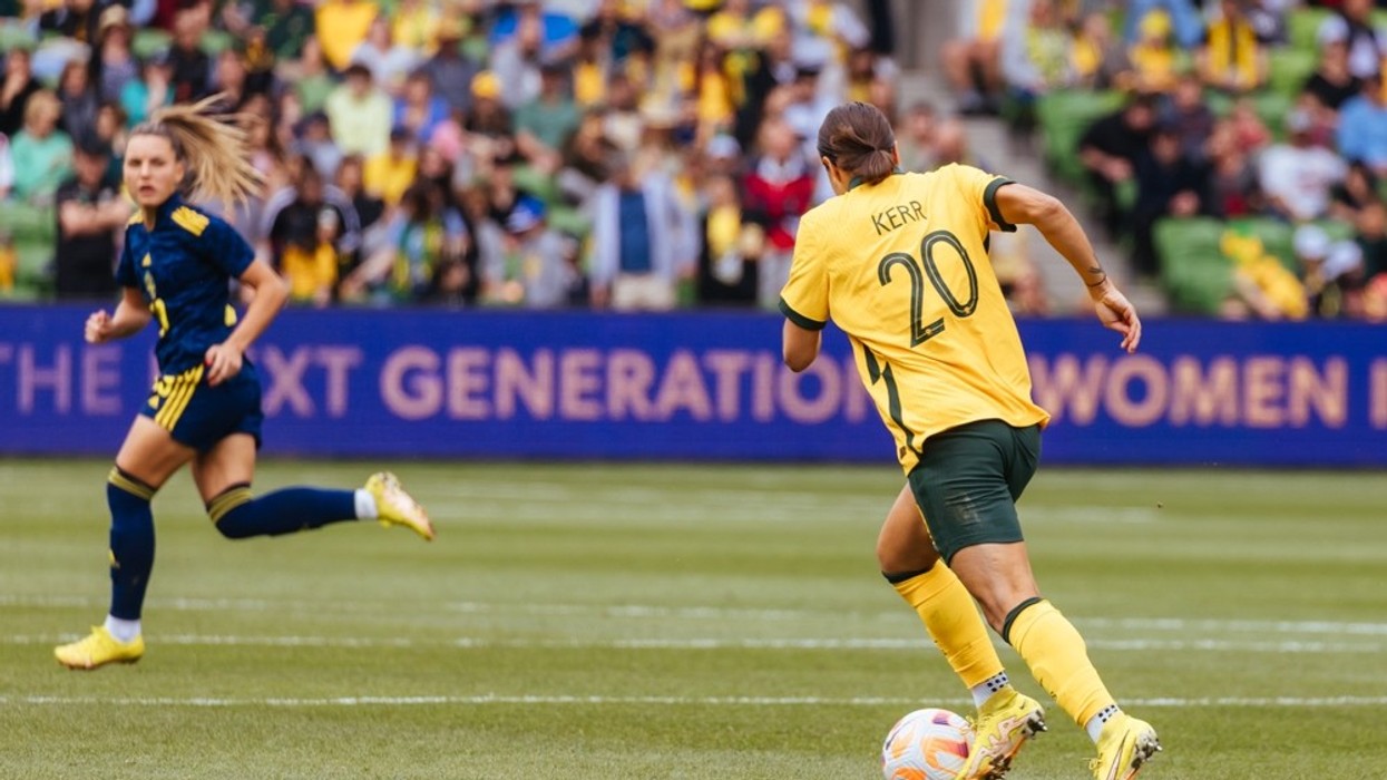 An action shot of football player Sam Kerr, wearing a yellow and green team uniform, with the ball