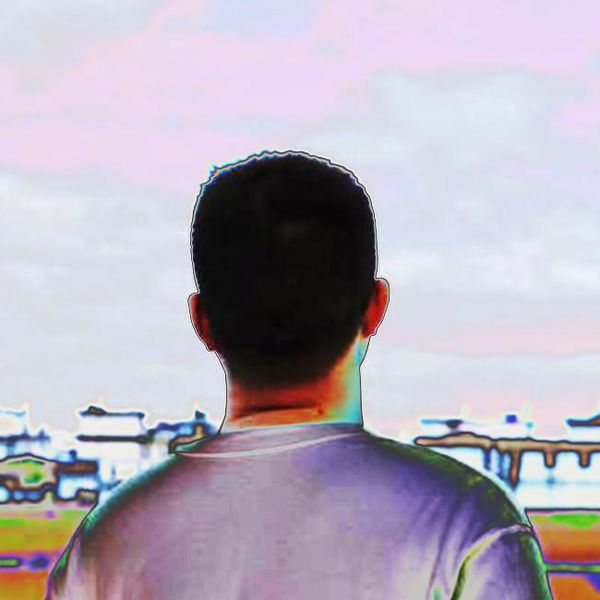 Back view of a young Chinese man looking at a row of houses in the distance.