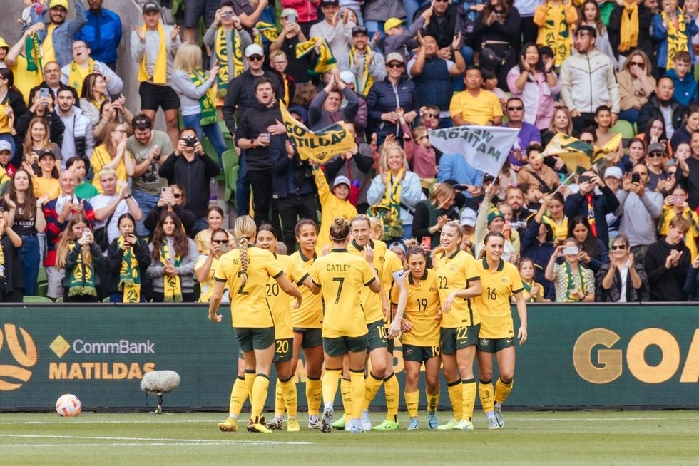 Female soccer players wearing yellow tops and green shorts celebrate a win