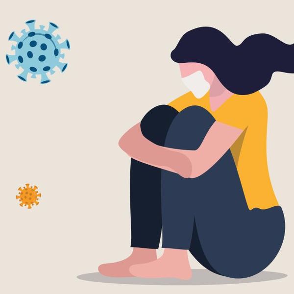 Illustration of a masked young woman sitting down with her arms wrapped around her raised knees. She is surrounded by floating COVID viral symbols.
