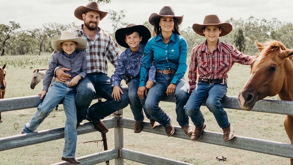  Image of mother, father and three pre-teen sons sitting on a stockyard rail in jeans and stockman hats.