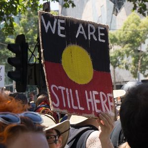 Indigenous rights protesters with sign "We are still here" held up.