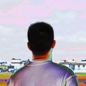 Back view of a young Chinese man looking at a row of houses in the distance.