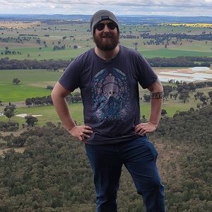 Young man standing on a rocky outcrop with wide view of farming land below him.