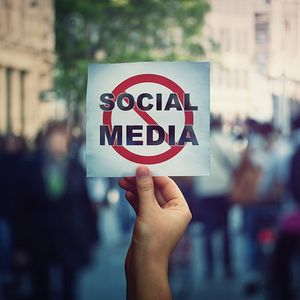 Image of a hand holding up a sign that reads social media with a red ircle and strike through line over the words.