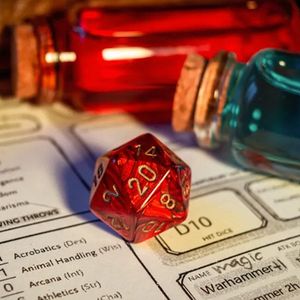 A multi-sided red die sits upon a character sheet for a Dungeons and Dragons game. Two bottles sit behind the die, one with blue liquid, the other with red.
