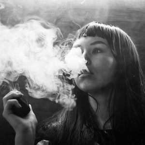 Black and white image of girl exhaling smoke from a vape.