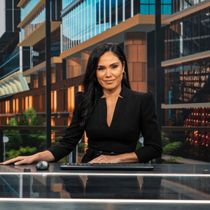 Woman sits behind a presenting desk in a tv studio