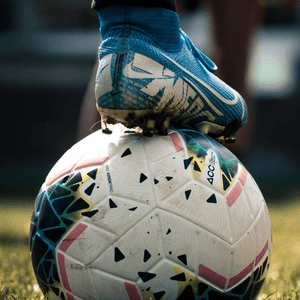 A man standing with a microphone, a foot on a football and a grey haired Iranian cleric