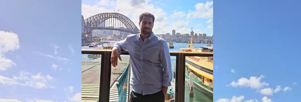 Man at Circular Quay standing with his back to the Sydney Harbour Bridge and the ferries