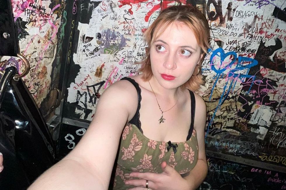 Photo of a young woman standing in front of a wall covered in graffiti.