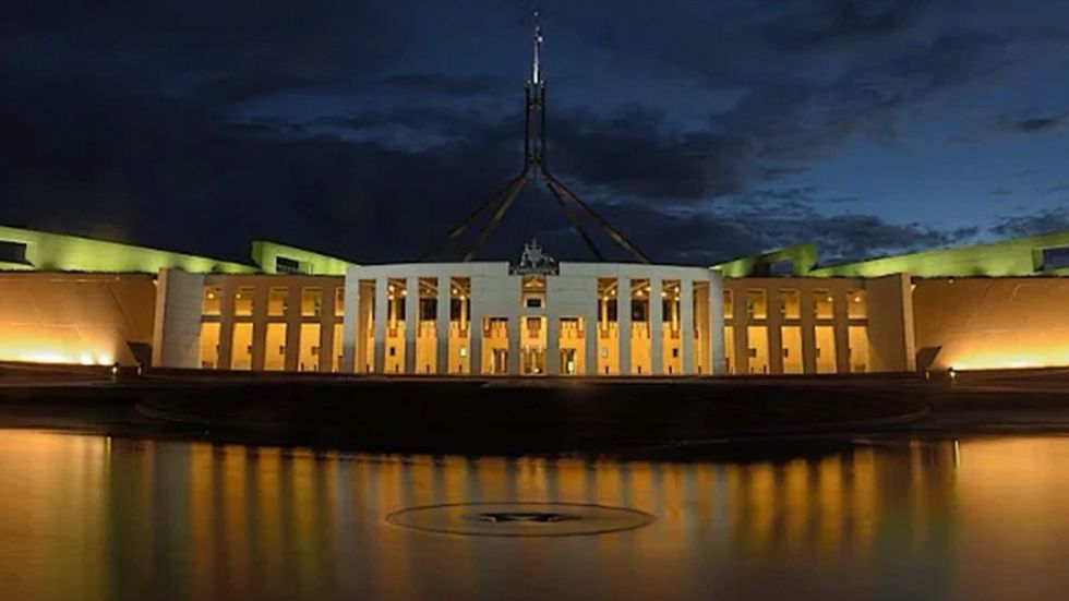 Picture of the front of Australian Parliament House lit up at night.