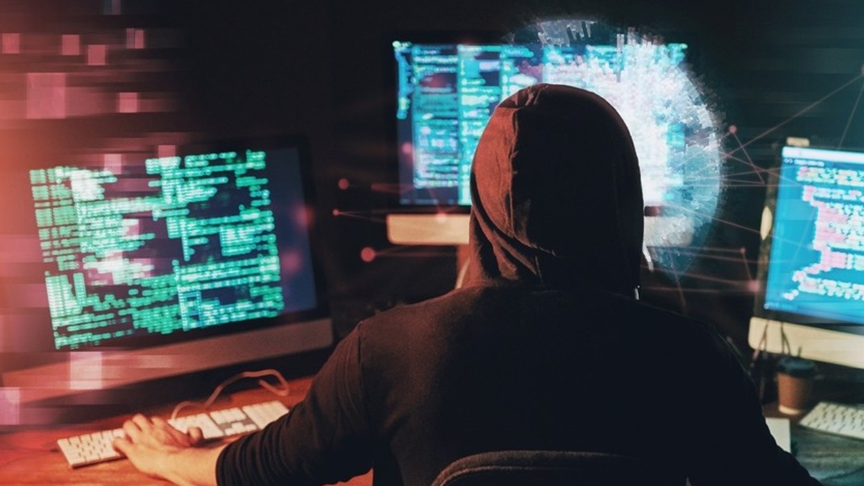 The back view of a man wearing a hoodie in front of three screens
