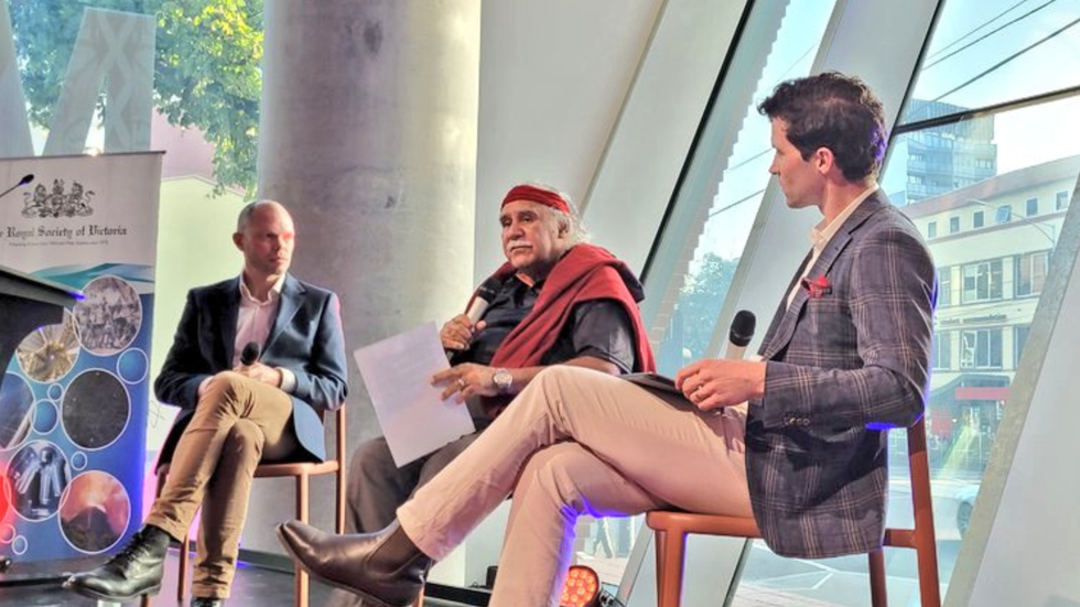 Three men sitting on a stage having a conversation.