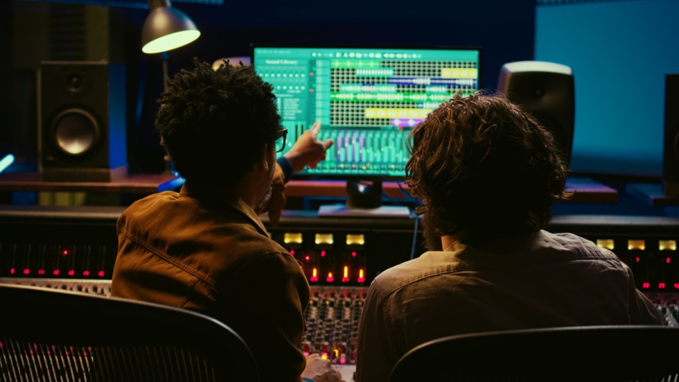 Two music engineers sit opposite screens
