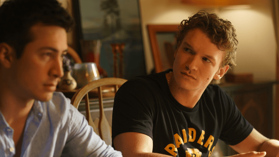 Two young men sitting at a table, one in a blue shirt, one in a black t-shirt