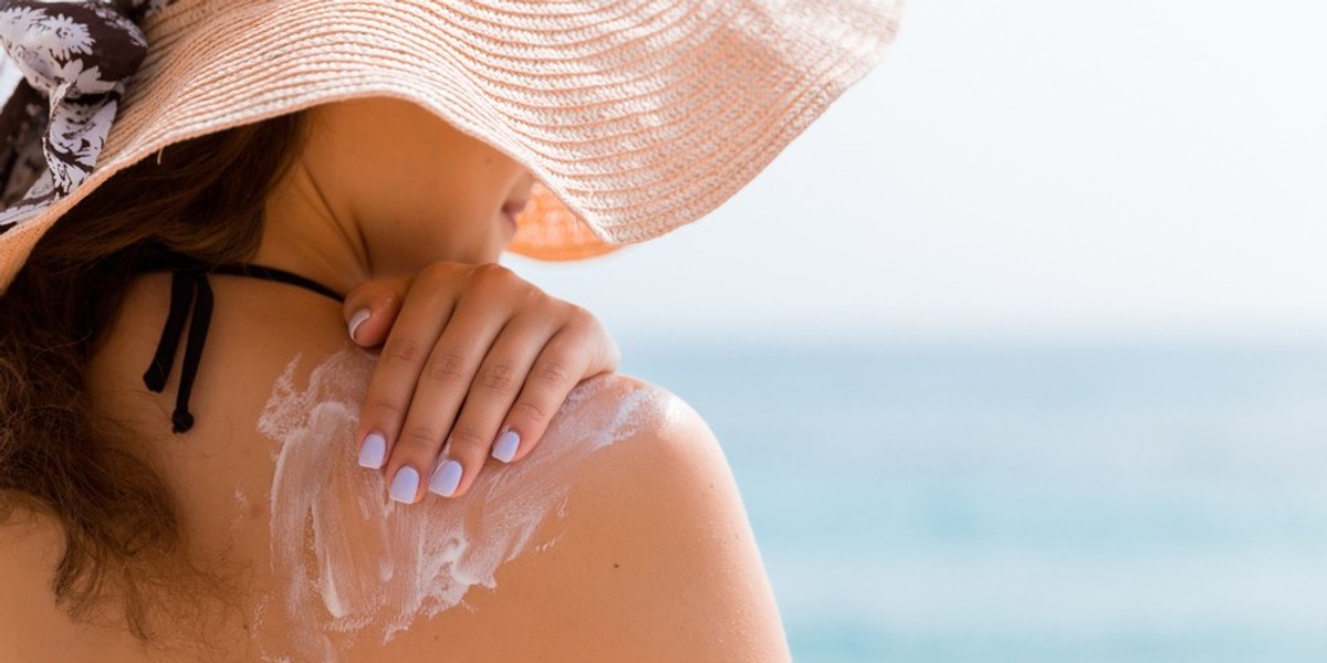 Woman in hat rubbing lotion on her back
