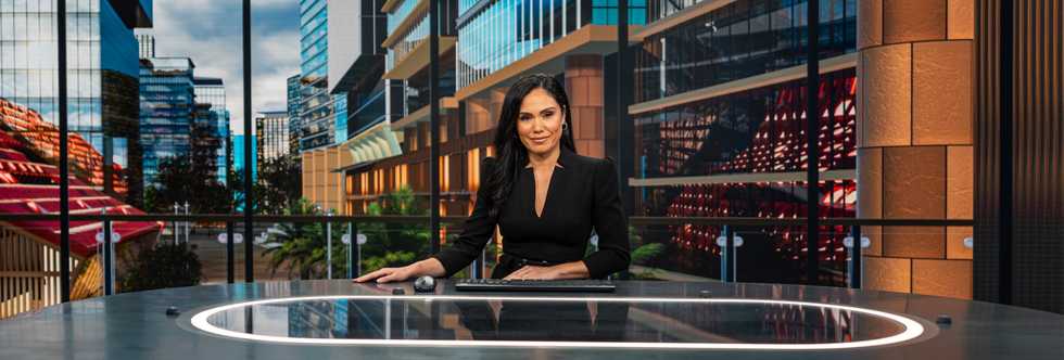 Woman sits behind a presenting desk in a tv studio