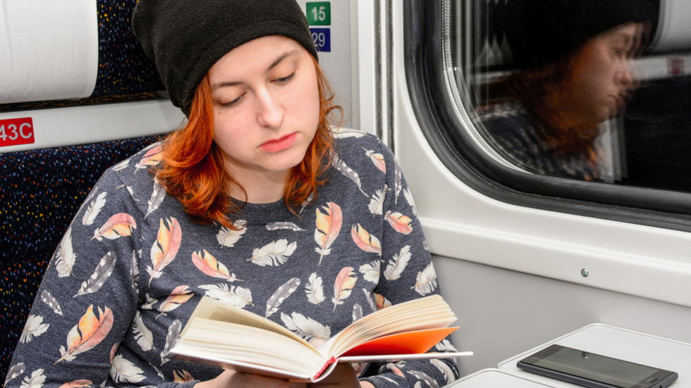 Woman with brightly coloured hair reading a book while on the train