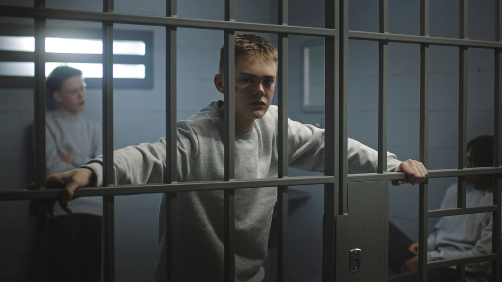 Young child standing behind prison bars holding on the rails