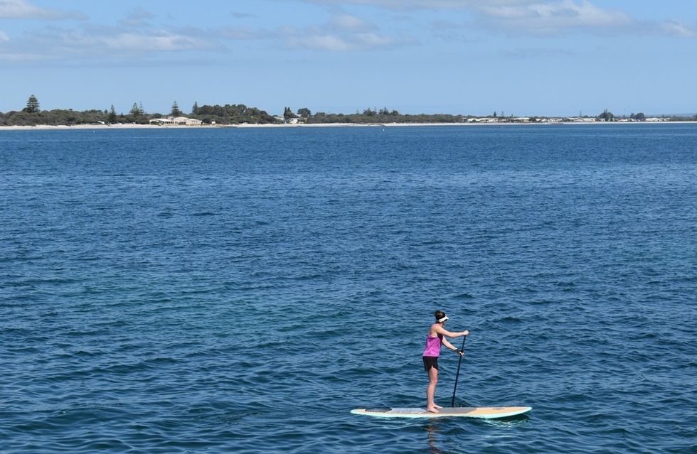 Young woman on paddle board in Geographe Bay with beach and seafront in background, Busselton, Western Australia, Australia